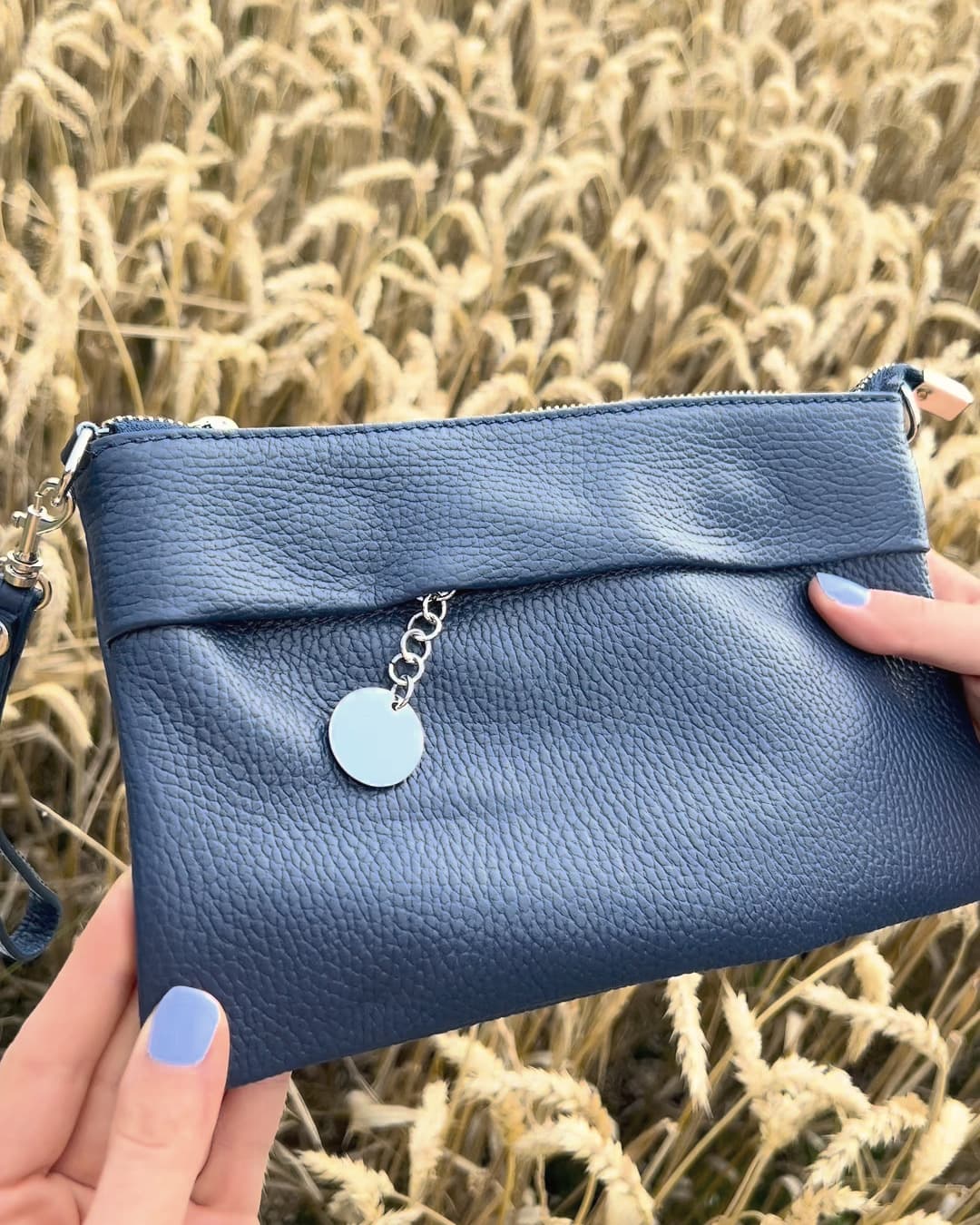 Vienna Mini Henkeltasche in der Hand, runde Metallplakette am Reißverschluss